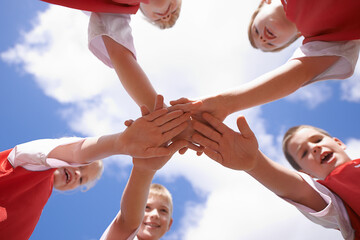 Hands, huddle and group of children on soccer team, team building and collaboration or support in circle. People, solidarity and team or partnership and trust in community, unity and sky background