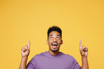 Poster - Young surprised man of African American ethnicity wears purple t-shirt casual clothes point index finger overhead on area mock up isolated on plain yellow background studio portrait Lifestyle concept