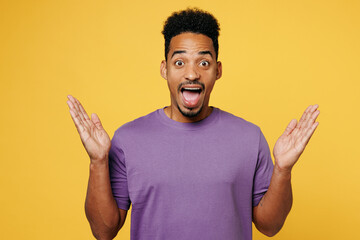 Wall Mural - Young surprised shocked happy man of African American ethnicity he wears purple t-shirt casual clothes spread hands look camera isolated on plain yellow background studio portrait. Lifestyle concept.