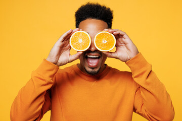 Wall Mural - Young happy man wear sweatshirt casual clothes hold in hand half of orange cover eye isolated on plain yellow background studio portrait. Proper nutrition healthy fast food unhealthy choice concept.