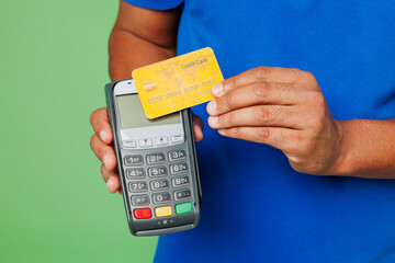 Poster - Cropped delivery guy employee man wears blue cap t-shirt uniform workwear work as dealer courier hold bank terminal to process acquire credit card isolated on plain green background. Service concept.