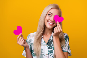 Wall Mural - Photo of girlish woman with straight hair dressed shirt holding pink heart on eye look empty space isolated on yellow color background