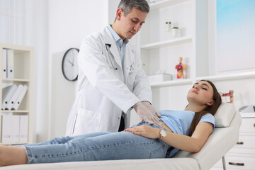 Canvas Print - Gastroenterologist examining patient with stomach pain on couch in clinic