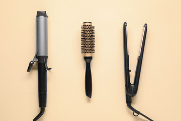 Wall Mural - Curling iron, hair straightener and round brush on beige background, flat lay