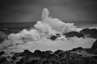 black and white image of large wave crashing onto rocks