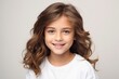 beauty, people and health concept - smiling little girl with long curly hair over grey background