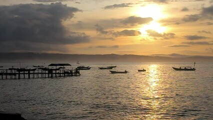 Wall Mural - Timelapse the view of the sunrise at Pangandaran beach harbor with the silhouette of a pier and several boats in the sea.