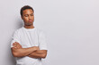 © wayhome.studio  - Sulking upset dark skinned man keeps arms folded being dissatisfied with something has sad thoughtful expression wears casual t shirt isolated over white background copy space for your promotion
