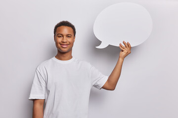 Wall Mural - People positive emotions concept. Studio shot of young happy smiling African american guy standing in centre isolated on white background holding speech bubble with blank space for advertisement