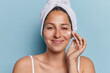 © wayhome.studio  - Beauty concept. Indoor shot of young happy satisfied European lady starting to wash applying soap on face after shower or bath with towel on head standing isolated in centre on blue background