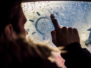 A person is looking out of a car window and drawing a sun on the fogged glass