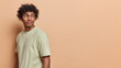 © WHstudio Leushin N - People emotions concept. Sideway photo of young happy satisfied Hindu man standing on left isolated on beige background looking at blank space for your promotion wearing white casual t shirt
