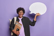 Waist up shot of cheerful Hindu man holds blank speech bubble notepads smartphone wears spectacles and black shirt carries backpack on shoulder isolated over purple wall. Write your ideas for studying