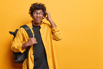Wall Mural - Indoor waist up of young confused Hindu male student standing on left on yellow background with blank space for your advertisement wearing shirt and t shirt with black bag after seeing test results