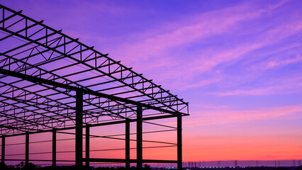 Wall Mural - Silhouette metal warehouse outline structure in construction site against colorful twilight sky background in industrial settlement area