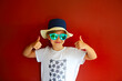 Pretty emothional child wear a hat and sunglasses on a red background