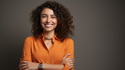 Wall Mural - Confident woman with curly hair, smiling at the camera, wearing a bright orange shirt, with her arms crossed.