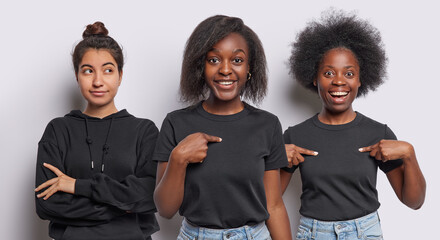 Wall Mural - Two African women have happy surprised expressions and point at themselves amazed to be chosen thoughtful Iranian girl keeps arms folded looks pensively aside all wear black clothing. Collage shot