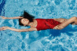 © SHOTPRIME STUDIO - Young woman in the pool in a red swimsuit with a beautiful smile lying on the water and swimming in the sun swimming in the pool, the concept of relaxing on vacation.