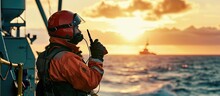Marine Deck Officer Or Chief Mate On Deck Of Offshore Vessel Or Ship Wearing PPE Personal Protective Equipment Helmet Coverall He Holds VHF Walkie Talkie Radio In Hands. Creative Banner
