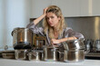 © Volodymyr - Too much housework. Sad woman with cooking pot. Woman with many cooking pots in the kitchen in the morning. Young upset woman cooking in kitchen.