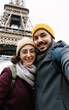 © Xavier Lorenzo - Vertical photo of young adult european couple taking selfie portrait with phone in front of Eiffel Tower in Paris city, France. Travel and vacation concept.