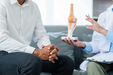 Wall Mural - male patient and male doctor discussing a model of a knee joint, likely focusing on condition of knee arthritis during a medical consultation.