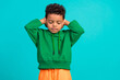 Photo of adorable nice schoolboy with wavy hair dressed green pullover arms cover ears eyes closed isolated on teal color background