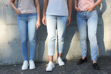 Women in stylish jeans near grey wall outdoors on sunny day, closeup