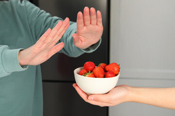 Wall Mural - Woman suffering from food allergies refusing offered strawberries by her friend at home, closeup