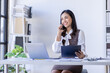 © David - Asian woman entrepreneur busy with her work in the office. Young Asian woman work on desk laptop phone while planning sales, research or financial strategy in company