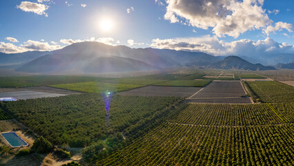 Wall Mural - Aerial view of fields with mountains in the distance and sun rays coming through the clouds.