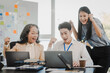 © makibestphoto - Asian office worker discussing with younger colleagues over laptops in a meeting room, possibly reviewing monthly reports or sharing opinions.