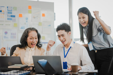 Wall Mural - Asian office worker discussing with younger colleagues over laptops in a meeting room, possibly reviewing monthly reports or sharing opinions.