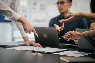 Wall Mural - diverse group of Asian professionals, including middle-aged and mature individuals, gathered around a table in a business setting, discussing documents with focused attention.