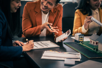 Wall Mural - Asian real estate team engaged in a discussion, with two men and a woman focusing on a house model on a table, suggesting a planning or sales meeting.