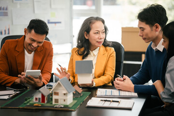 Wall Mural - Asian real estate team engaged in a discussion, with two men and a woman focusing on a house model on a table, suggesting a planning or sales meeting.