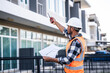 © Ratirath - engineer in a high-visibility vest and hard hat, intently reviewing a document or blueprint, with a modern building in the background.