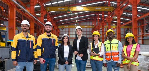 A smiling team of worker stand together for a group photo inside a factory with machinery in the background.