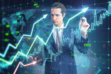 Attractive young european businessman with laptop using growing upward chart, map, arrows and forex graph on blurry background. Global trends, trading and finance concept. Double exposure.