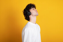 Young man listening to music with eyes closed against yellow background