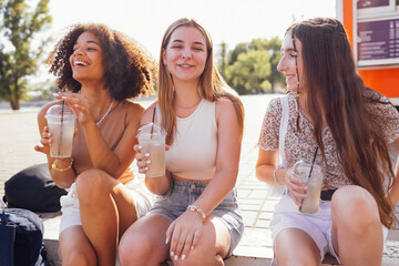 Wall Mural - Cute teenage girls in casual summer clothes drinking tasty iced lemonade outdoors in the park.