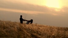 Silhouette Of A Couple In A Golden Field And A Beautiful Sunset. A Young And Romantic Family Enjoys Each Other's Company. Love On A Summer Evening.