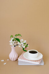 Wall Mural - Festive spring greeting card on a beige background. A cup of tea in a white porcelain cup, apple blossoms and books