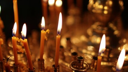 Wall Mural - Close up burning candles in the Orthodox church. Memorial wax candles flicker with fire flame on large gold candlestick in the temple against dark. Concept of religion and faith in god