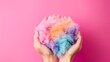 A view from above shows a hand holding colorful wool on a pink background.