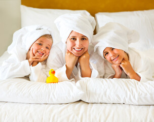 Wall Mural - Happy mother and girls in bathrobes on bed