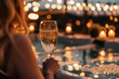 rear view of a woman holding glasses of champagne in front of a lightened pool area.