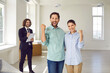 © Studio Romantic - Portrait of a young excited smiling family couple happy about buying a new apartment standing with man realtor in new house making yes gesture enjoying real estate purchase. Moving day concept.