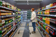 © wifesun - Man in store among racks of sodas. Young stylish millennial guy shopping in supermarket. Concept of huge selection of products, trip to hypermarket on sunday weekend. Promotions and discounts